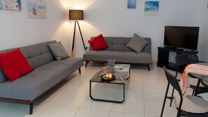 Un salon moderne avec un canapé gris, des coussins rouges, une table basse avec des bougies et un meuble pour la télévision.