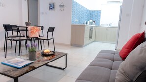 Un salon moderne avec un canapé gris, une table basse sur laquelle sont posés des magazines et un coin repas comprenant des chaises et une petite table.