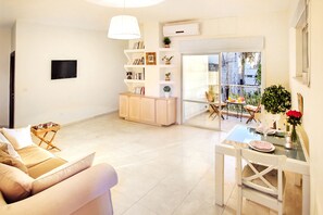 Una sala moderna con un sofá, una mesa de comedor con sillas, una estantería y un ventanal corredizo que da a un balcón al aire libre.