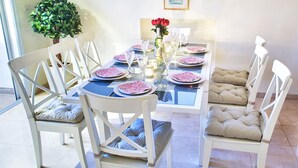 A dining table set with plates, glasses, and a bottle, surrounded by white chairs with cushioned seats. - 2 BDR with Balcony ► Best Location: German Colony - Shelter in the building (Jerusalem)