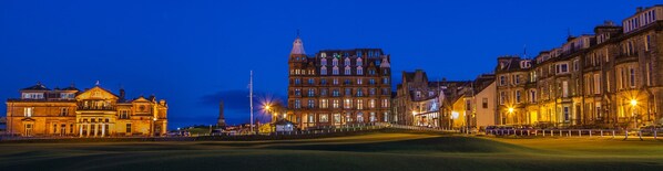 Un edificio histórico con arquitectura clásica, un césped cuidado y un cielo nocturno despejado.