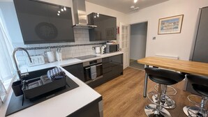 Een moderne keuken met een spoelbak, fornuis en magnetron. Er is een eethoek met een houten tafel en barkrukken.