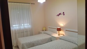 Habitació amb dos llits, una tauleta de nit, una làmpada i un lluminari fixat a la paret.