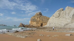 Una platja rocosa amb un penya-segat gran i una persona a prop de l'aigua.