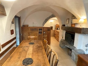 Un coin repas rustique avec une table et des chaises en bois, une cheminée en pierre et une cuisine en arrière-plan.