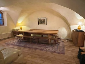 Un coin repas chaleureux avec une table et des bancs en bois, un tapis à motifs et une lampe sur une petite table d’appoint.