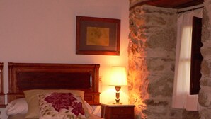 Une chambre avec un lit en bois, une table de chevet avec une lampe, un mur en pierre et une fenêtre avec des rideaux.