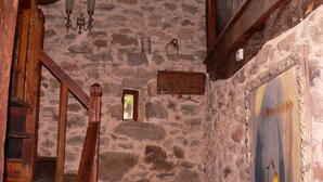 Une pièce aux murs de pierre, avec un escalier en bois, une petite fenêtre et un tableau encadré accroché au mur.