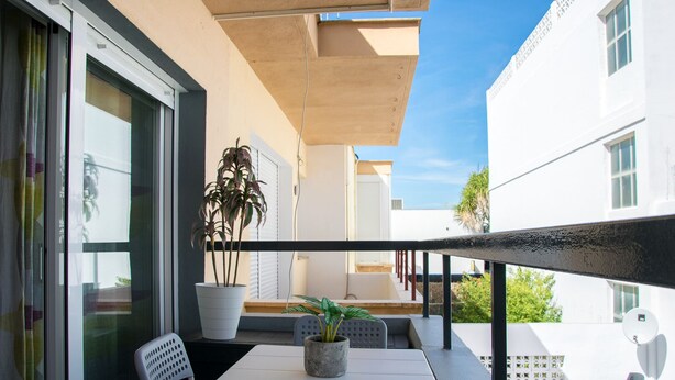 A balcony with a table and chairs, potted plants, and a view of adjacent buildings. - LOS NARANJOS APARTMENT.  (Matalascañas)