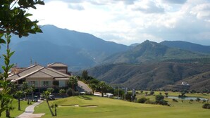 A golf course with a clubhouse, palm trees, and mountains in the background.