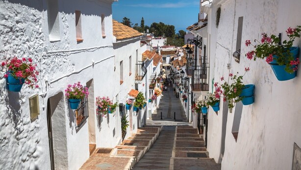 A narrow street with white buildings, stone steps, and hanging flower baskets.