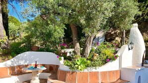A landscaped outdoor area with a curved seating area, a small table with a bottle and glasses, and a decorative lamp post.