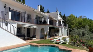 A two-story house with a swimming pool, outdoor seating, and a garden.