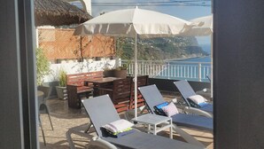 A balcony with lounge chairs, a table, and a thatched roof structure.
