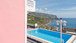 A pool with a view of a coastal landscape, including a beach and cliffs.