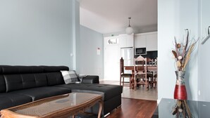 A modern living room with a black sectional sofa, a wooden coffee table, and a dining area with wooden chairs and a white table.