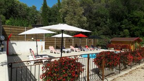 A pool area with lounge chairs and umbrellas, surrounded by a wooden fence and red flowers. - House / Villa - Draguignan (Draguignan)