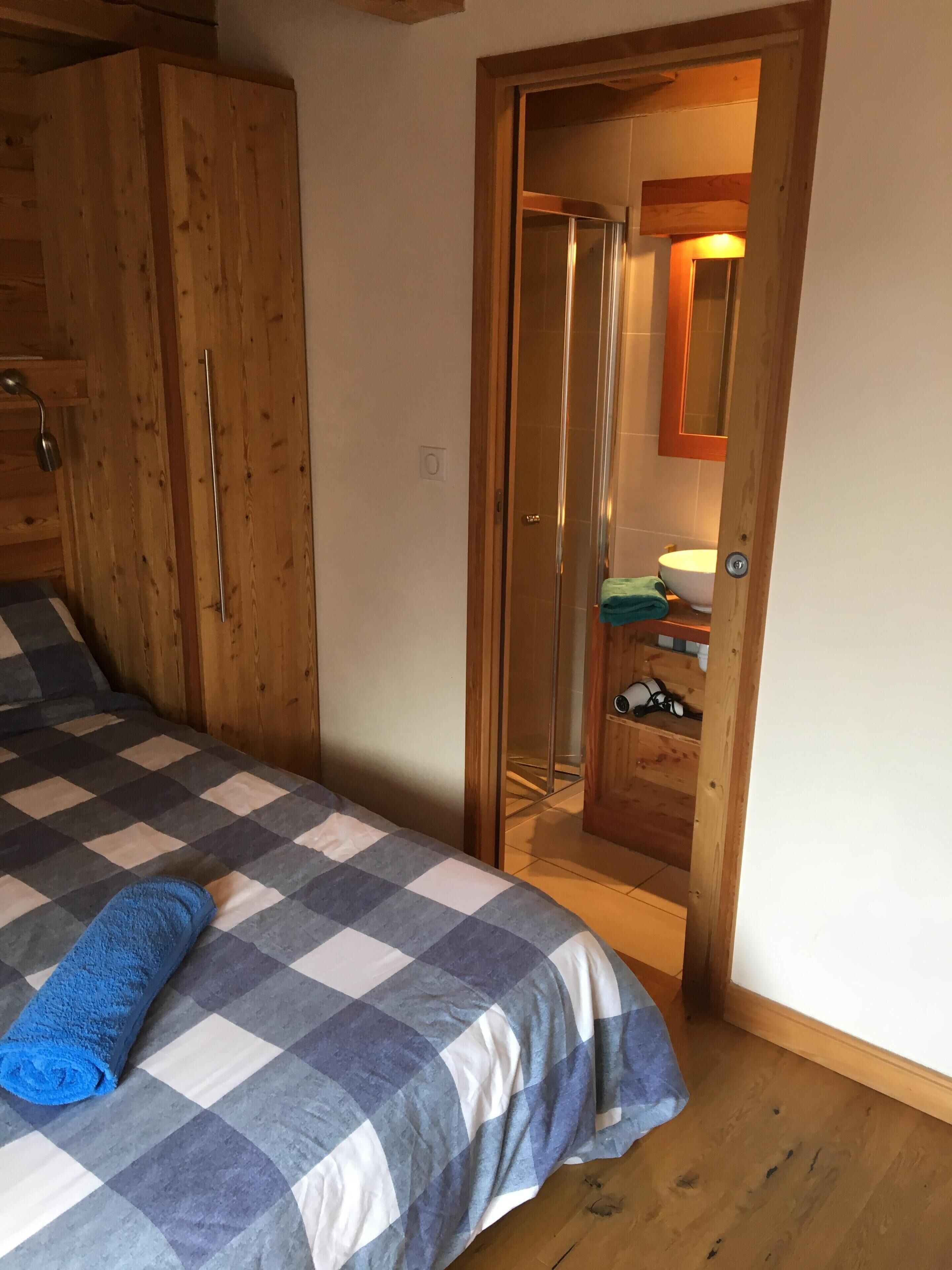 Une chambre à coucher avec une couvre-lit à carreaux, une armoire en bois et une salle de bain visible à travers une porte.