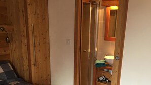 A bedroom with a checkered bedspread, wooden wardrobe, and a bathroom visible through a door.