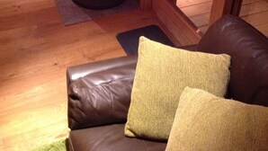 A cozy room with a fireplace, wooden flooring, and a leather sofa with cushions.