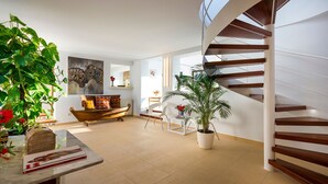 Un salon moderne avec un escalier en bois, une grande plante en pot et un coin repas comprenant une table et des chaises en bois.