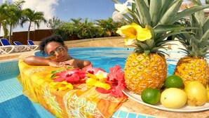 A poolside area with a person relaxing on a colorful lounge chair, a plate of fruits, and a tropical setting with palm trees. - Exclusive Ocean View Suite Villa Esmeralda with Panoramic Pool (Las Galeras)