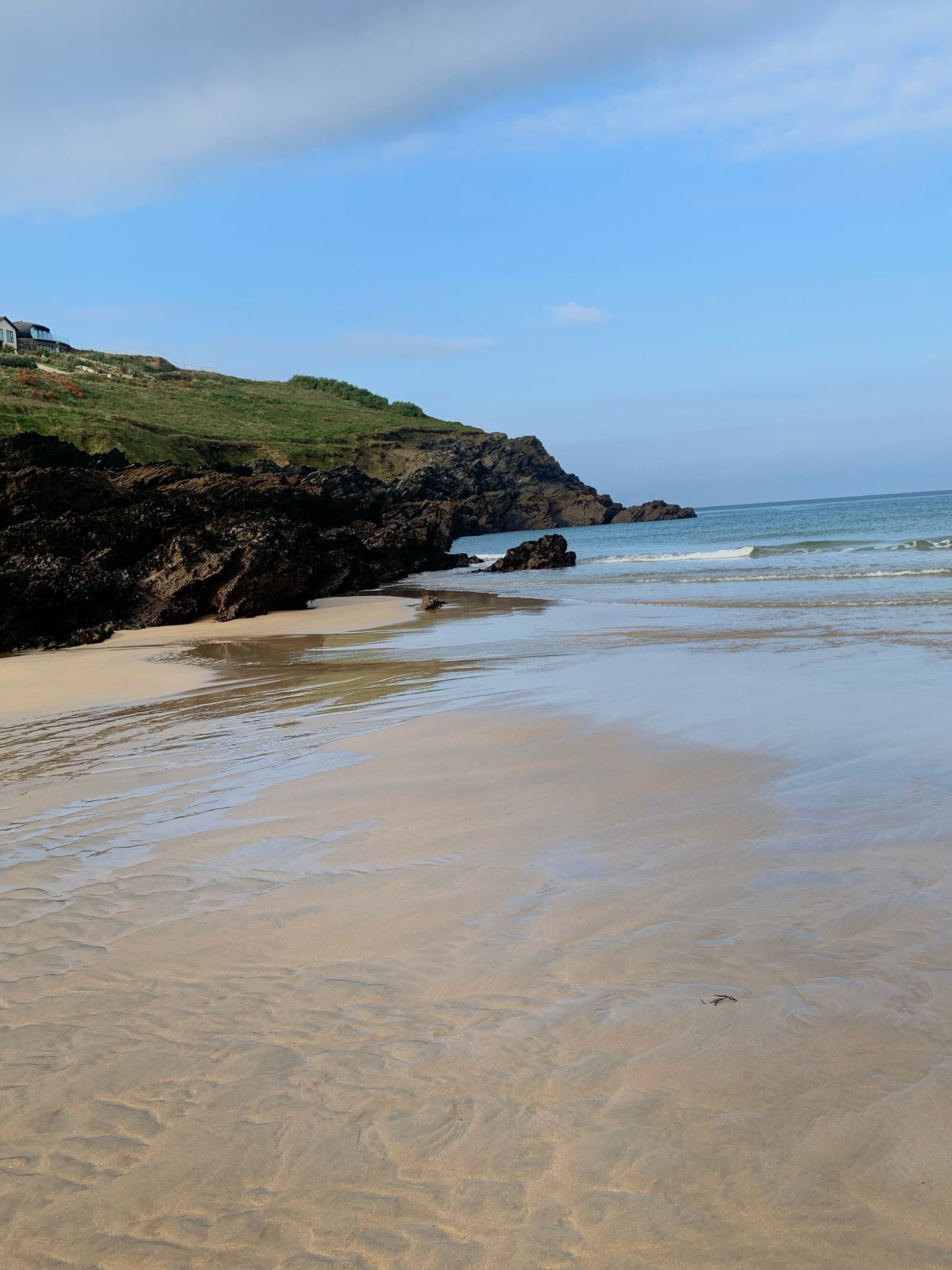 A beach with a rocky shoreline, a grassy hill, and a clear sky.