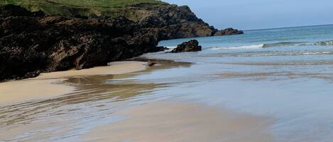 A beach with a rocky shoreline, a grassy hill, and a clear sky.
