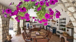 Een landelijke stenen keuken met houten meubels, een eettafel en paarse bloemen die aan het plafond hangen.