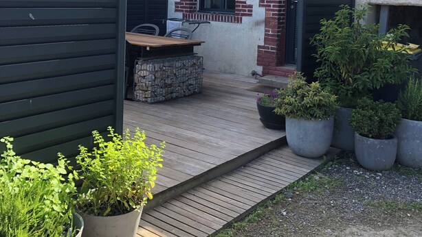 A house with a patio area featuring a wooden table and chairs, surrounded by potted plants.