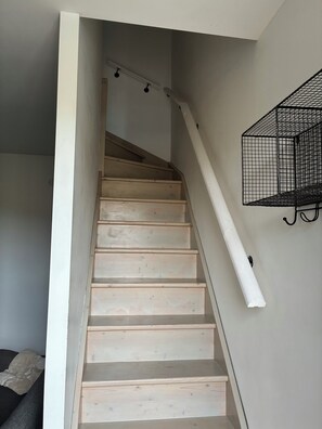 Een trap met houten treden en een witte leuning, die uitkomt op een plateau met een zwart metalen plank.