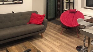 A modern living room with a grey sofa, a red chair, a wooden coffee table, and a dining area with a metal chair and table.