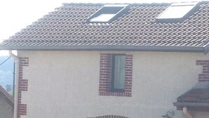 A two-story house with a tiled roof, brick accents, and a front porch with potted plants.