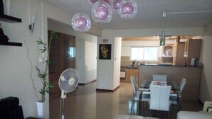 Un salon moderne avec un canapé blanc, un ventilateur sur pied et un coin repas comprenant une table et des chaises.