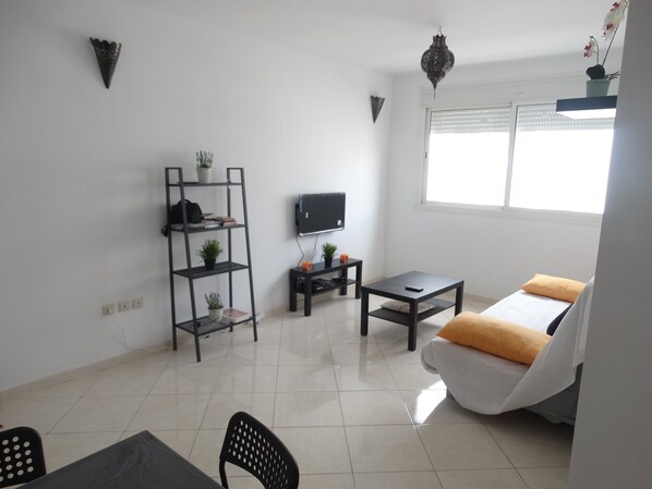 A modern living room with a sofa, a coffee table, a TV, and a bookshelf.