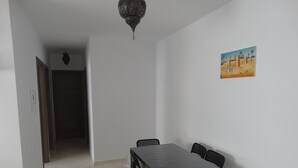 A dining area with a table and chairs, a hanging light fixture, and a painting on the wall. - apartment 6 person 10 minutes from the beach (agadir)
