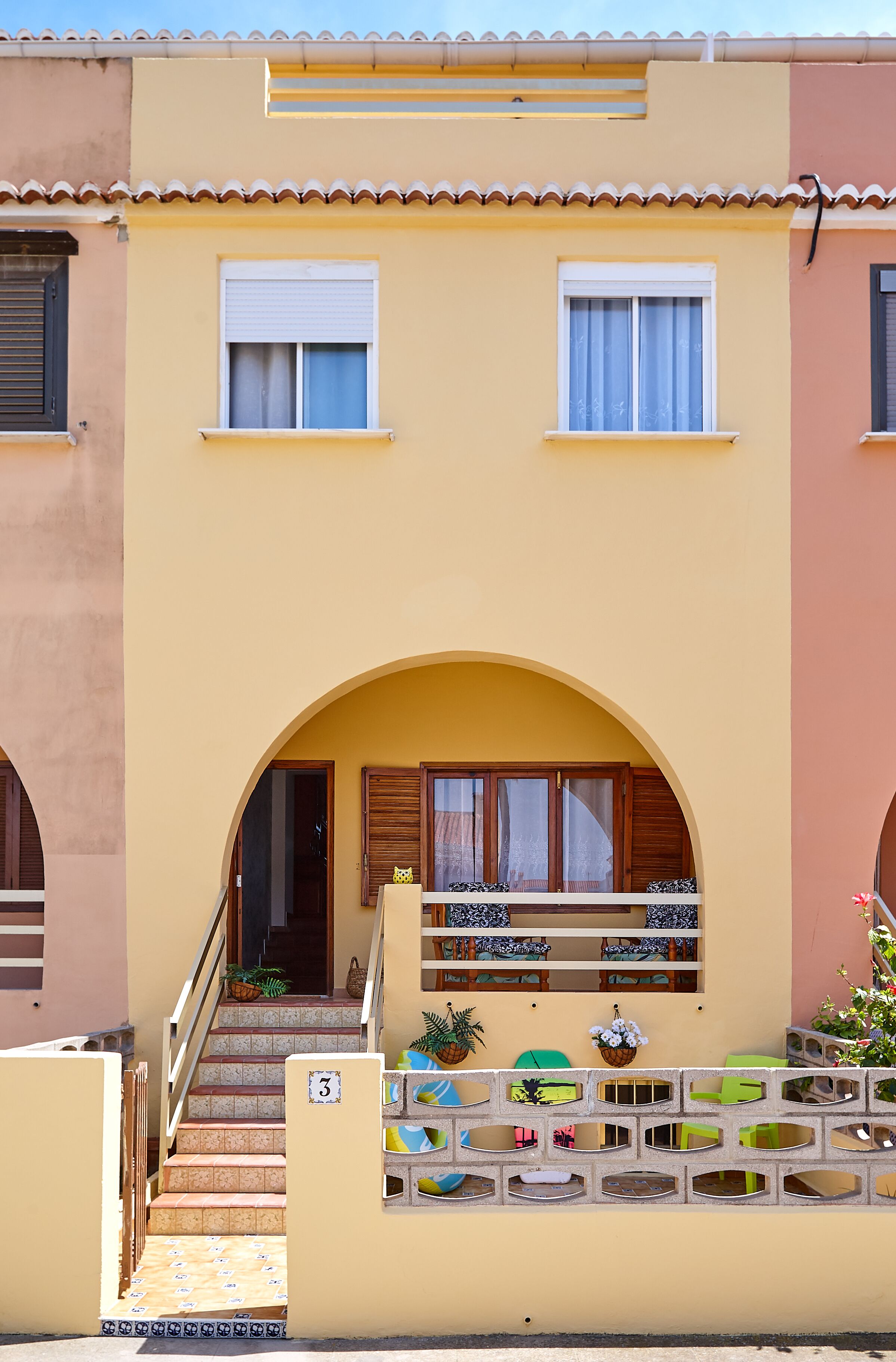 A two-story building with a yellow facade, a balcony with a tiled floor, and a staircase leading to the entrance.