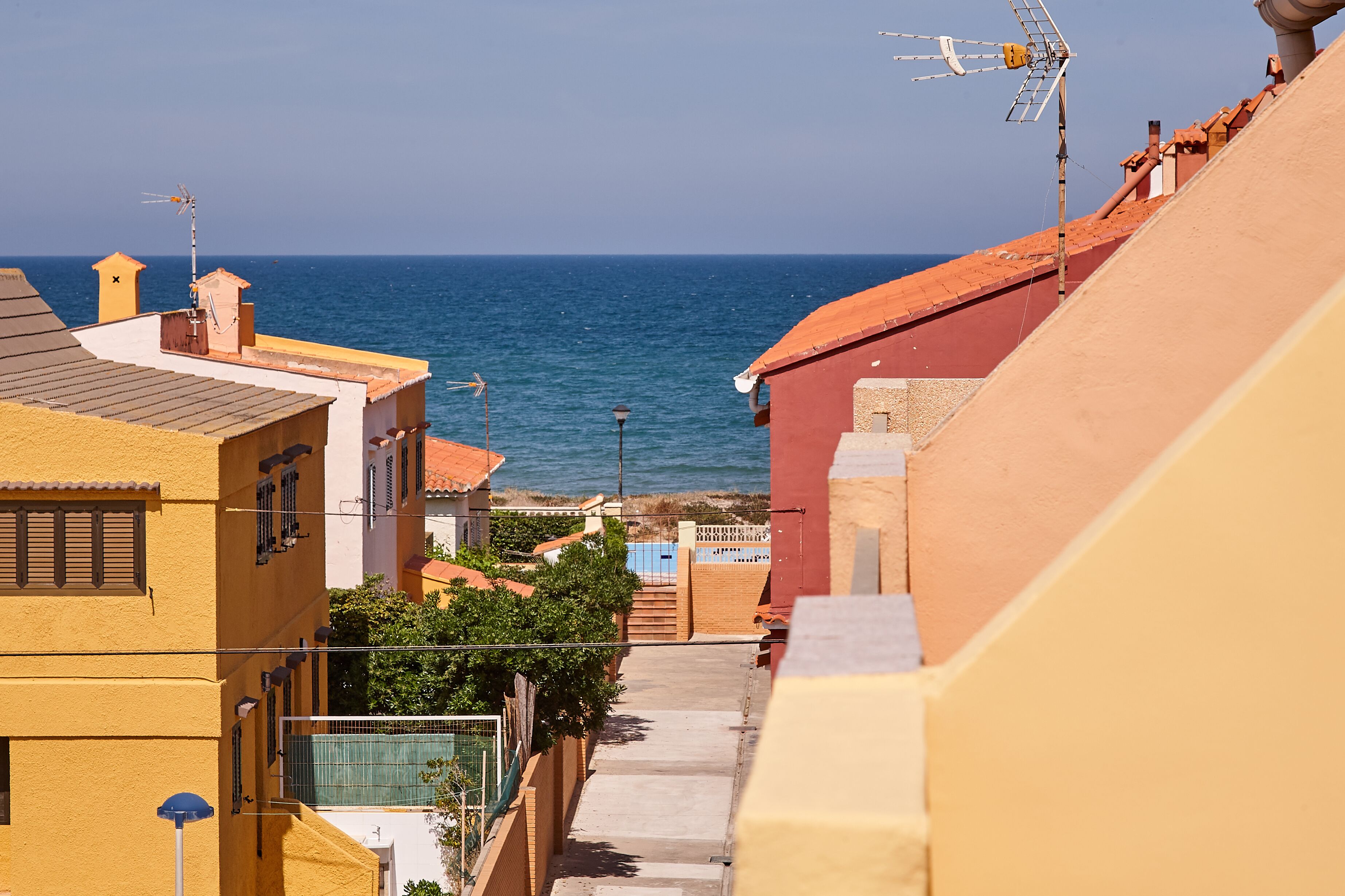 A coastal residential area with buildings, a clear view of the sea, and a staircase leading down to the beach.