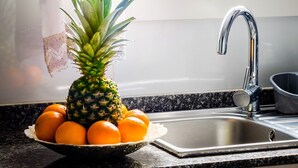 A kitchen with a sink, a window with a view of palm trees, a pineapple, and oranges on the counter. - Chalet on the beach Valencia Mareny Sueca Cullera (Mareni de Barraquetes Sueca)