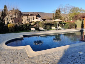 A swimming pool with stone tiles, lounge chairs, and umbrellas.