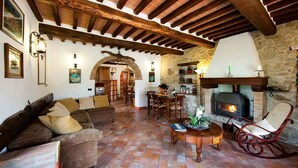 A rustic interior with a stone fireplace, wooden beams, a cozy seating area with a sofa and chairs, and a dining table. - Large country apartment in Cortona 3bed3bath with shared pool & gorgeous gardens (Cortona)
