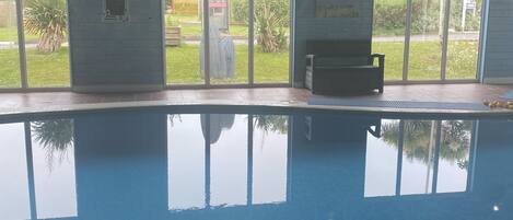 An indoor swimming pool with clear glass walls, a bench, and a clock on the wall.