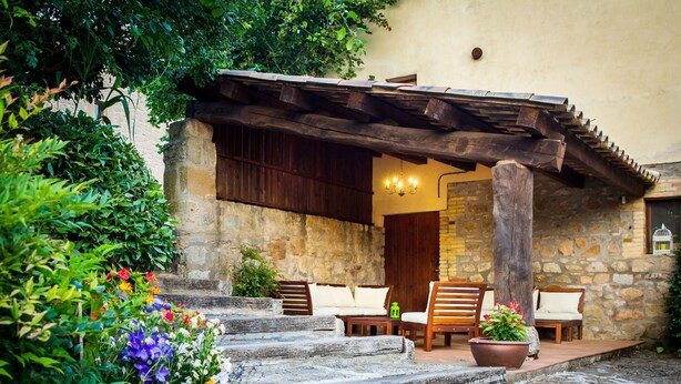 A stone building with a wooden pergola, outdoor seating, and a variety of flowers. - Casa Corral for 4 people (Lladurs)
