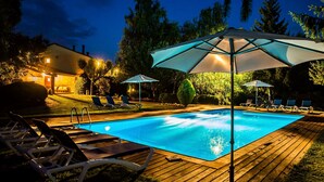 A swimming pool with lounge chairs and umbrellas, surrounded by a wooden deck and greenery. - Casa Corral for 4 people (Lladurs)