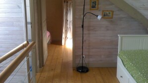 A room with a wooden floor, a bed with a green bedspread, a standing floor lamp, and two framed pictures on the wall. - the barn of Paul, seasonal rental in the peninsula of Rhuys (Le Hézo)