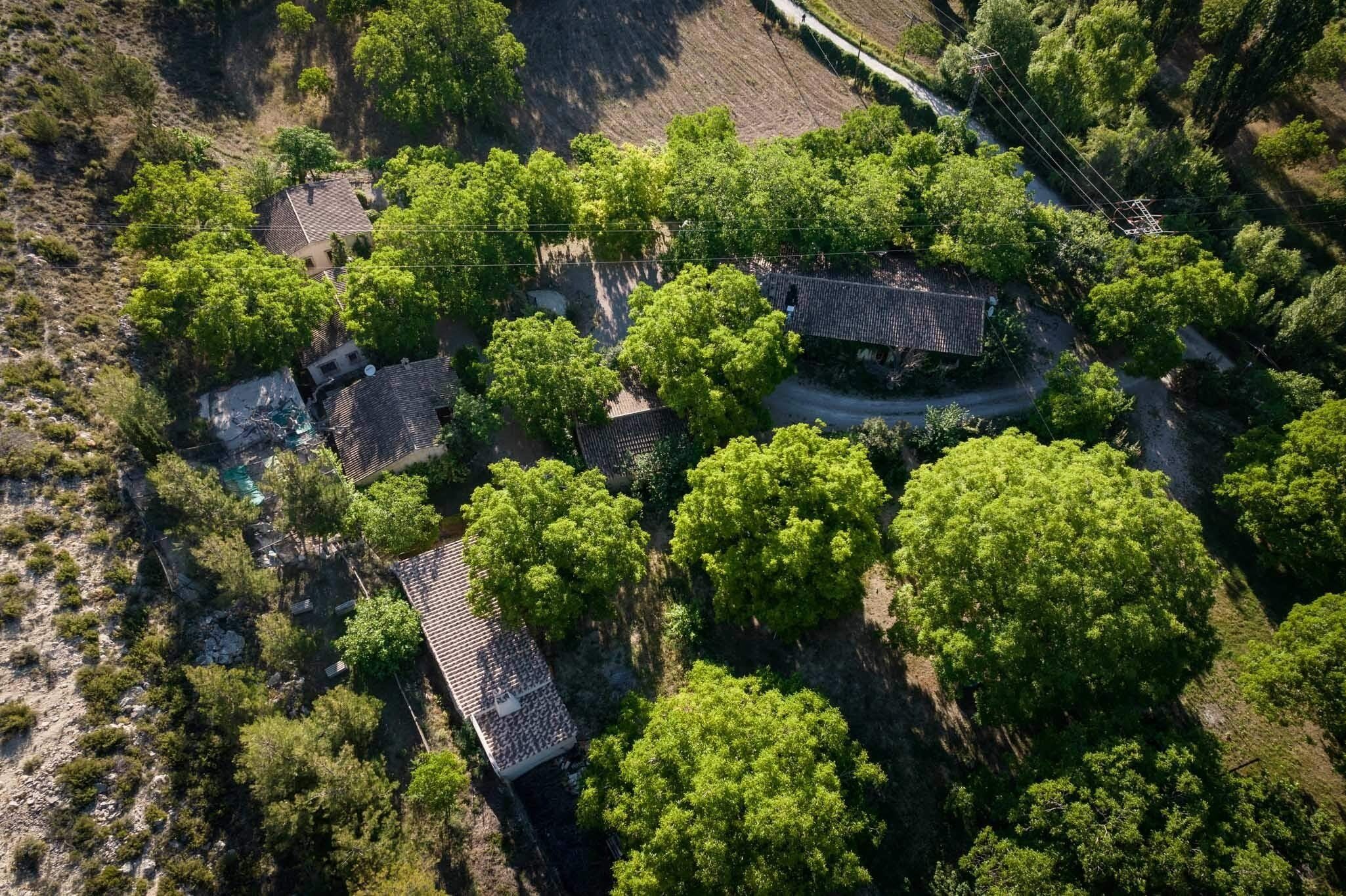 Oversigtsbillede fra luften af en landejendom med flere bygninger omgivet af frodig vegetation.