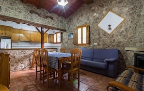 A rustic kitchen with stone walls, wooden cabinets, and a dining table with chairs.