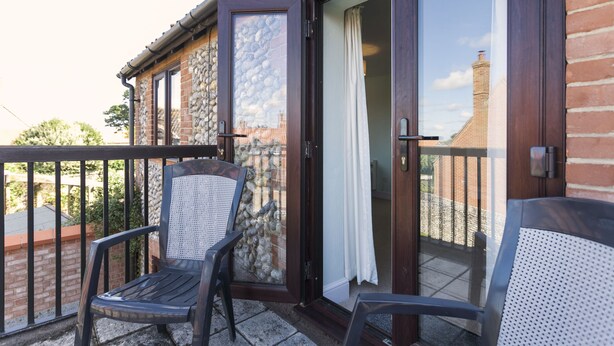 Un balcon avec deux chaises, un mur en pierre et une porte-fenêtre coulissante.