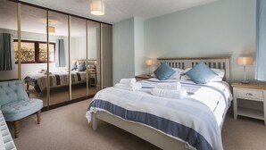 Une chambre avec un grand miroir, un lit avec une literie bleue et blanche, une table de chevet avec une lampe et une chaise.