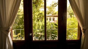 Una ventana con cortinas blancas, vista a una casa y un balcón con barandilla.